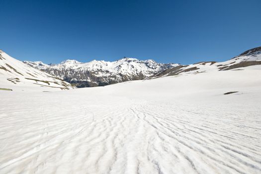 Snowy slope with melting grooves in scenic high mountain background and sunny spring day