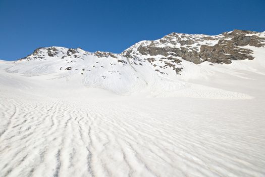 Snowy slope with melting grooves in scenic high mountain background and sunny spring day