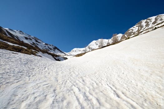 Snowy slope with melting grooves in scenic high mountain background and sunny spring day