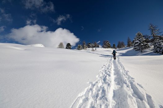 Alpinist hiking on snowy slope in scenic high mountain landscape, italian Alps