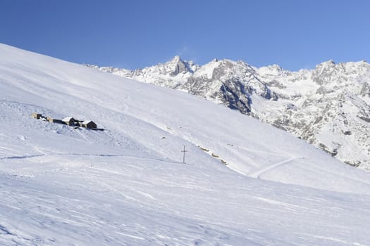 Winter landscape in the italian Alps with abandoned pasture huts covered by snow in scenic high altitude background (Gran Paradiso National Park).