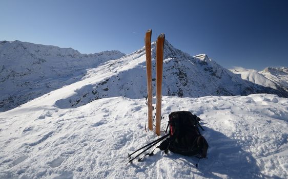 On the top of the mountain, pair of back country - tour ski and a backpack with avalanche safety tools. Scenic high mountain background (Gran Paradiso peak, 4061 m).