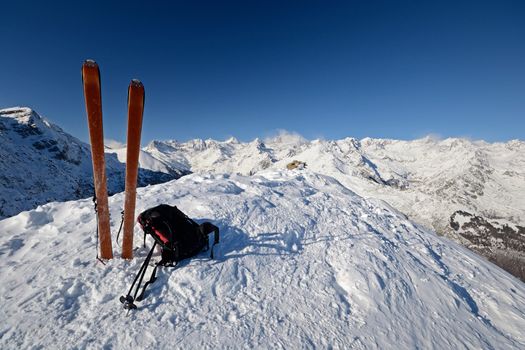 On the top of the mountain, pair of back country - tour ski and a backpack with avalanche safety tools. Scenic high mountain background (Gran Paradiso peak, 4061 m).