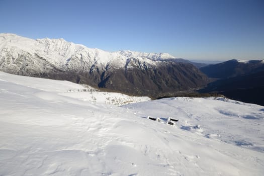 Winter landscape in the italian Alps with abandoned pasture huts covered by snow in scenic high altitude background (Gran Paradiso National Park).