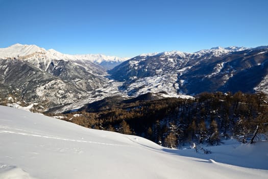 Winter landscape in the italian Alps in a bright day, with pure powder snow in the foreground and snow capped mountain peaks in the background