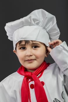 Little boy preparing healthy food on kitchen over grey background, cook hat