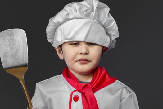 Kitchen, little boy preparing healthy food on kitchen over grey background, cook hat