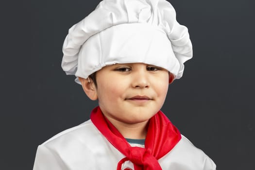 Little boy preparing healthy food on kitchen over grey background, cook hat