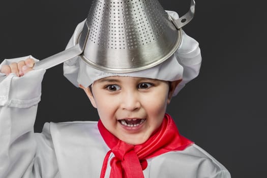 Little boy preparing healthy food on kitchen over grey background, cook hat