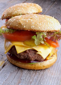 Two Tasty Hamburgers with Beef, Tomato, Lettuce, Pickle, Red Onion, Cheese and Sesame Buns closeup on Rustic Wooden background