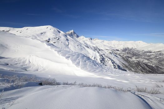 Candid off-piste ski slope in scenic background of mountain peaks, valleys and plain. Piedmont, Italian Alps