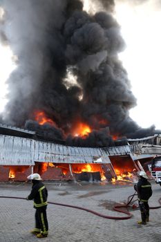 Warehouse building burning with intense flames and fireman attending