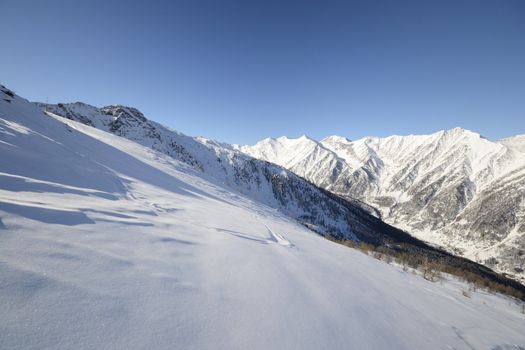 Candid off-piste ski slope in scenic background of mountain peaks, valleys and plain. Piedmont, Italian Alps