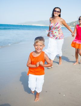 Adorable happy boy with sister and mother running on beach