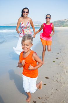 Adorable happy boy with sister and mother running on beach