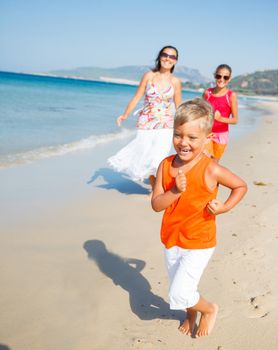 Adorable happy boy with sister and mother running on beach