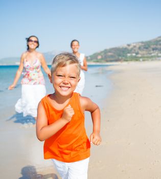 Adorable happy boy with sister and mother running on beach