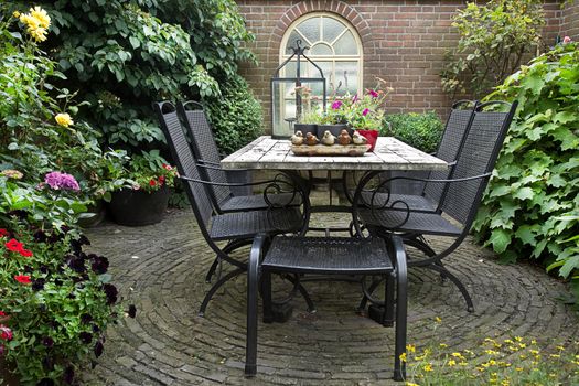 Iron forged table and chairs in garden with flowers, table decoration and potplants in summer