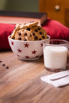 Closeup of chocolate chip cookies on stars bowl and milk glass over a wooden background