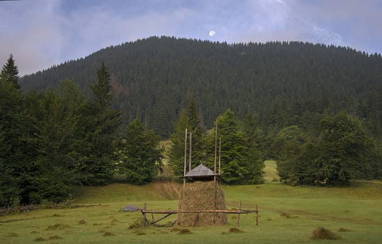 stack of slanted hay on a glade among mountains with the moon