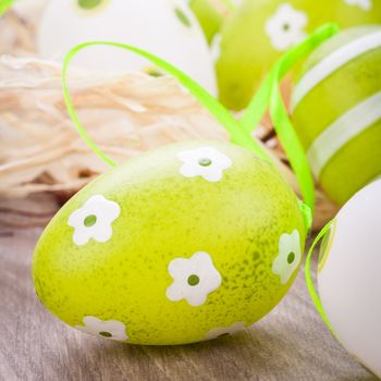 Collection of four hand decorated colourful green Easter eggs with different patterns displayed in straw, close up view