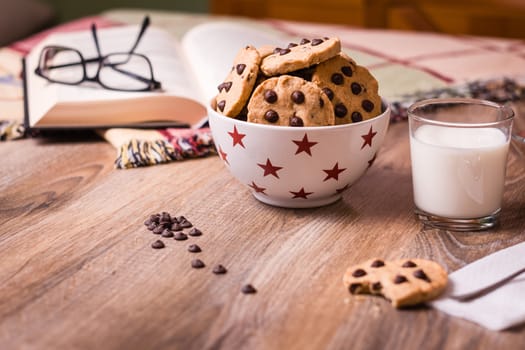 Closeup of chocolate chip cookies on stars bowl and milk glass over a wooden background