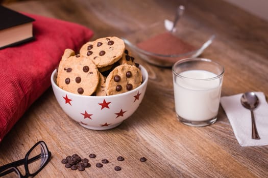 Closeup of chocolate chip cookies on stars bowl and milk glass over a wooden background