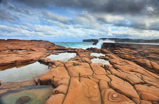 Ocean waves splash against spectacularrock formations at North Avoca, NSW Australia, with serene rockpools in the foreground.  