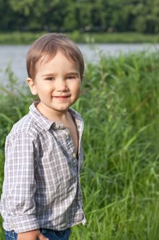 Little boy play in green grass near the river