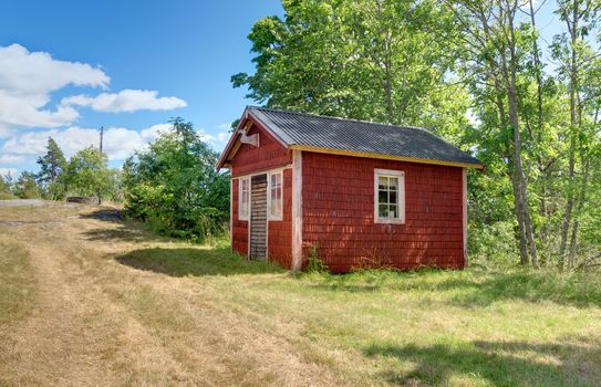 Traditional Swedish cabin painted in red color. Countryside in summer.
