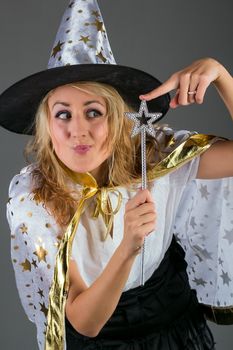 Young witch with magic wand at grey background