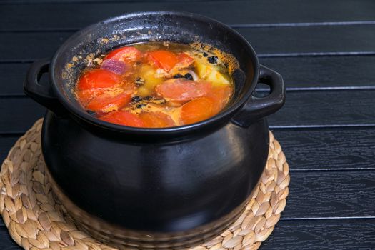 Soup in the black saucepan at wooden table