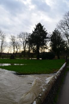 An English river is at capacity due to torrential rain and bursts its banks.