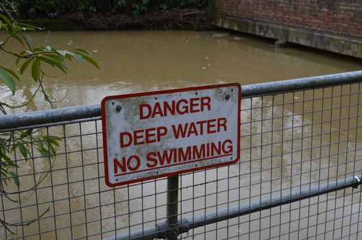 On the side of a riverbank a warning sign informs people of deep water and that swimming is forbidden.