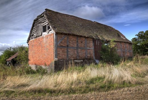Overgrown timber-frame and brick half-hipped barn, Warwickshire, England.