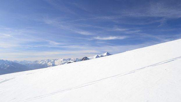 Candid off-piste ski slope in scenic background of mountain peaks, valleys and plain. Piedmont, Italian Alps