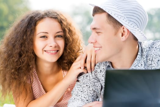 couple lying together in a park, working together on a laptop