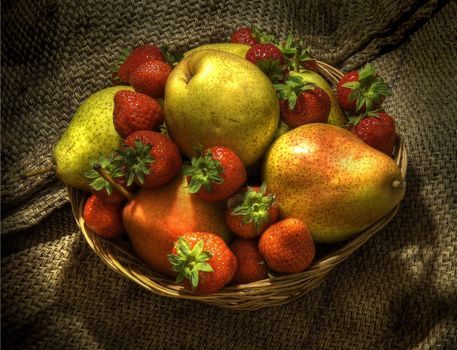 Pears and strawberries in a wicker basket on hessian.