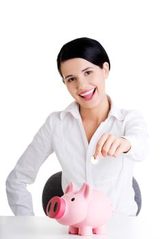 Happy businesswoman putting an euro coin into a piggy bank isolated on white background