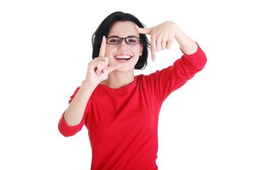 Smiling woman wearing red blouse is showing frame by hands. Happy girl with face in frame of palms. Isolated on white background.