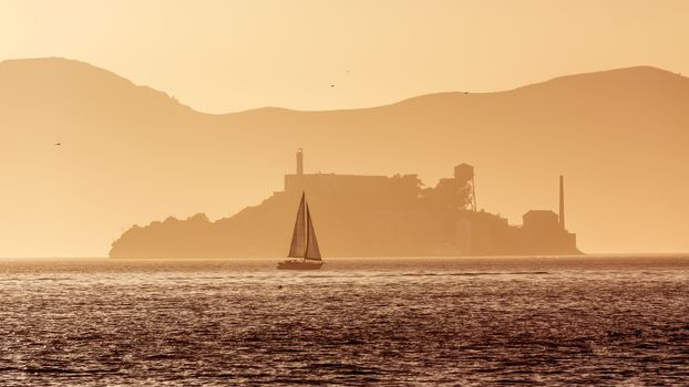 Alcatraz island penitentiary at sunset backlight sailboat in san Francisco California USA