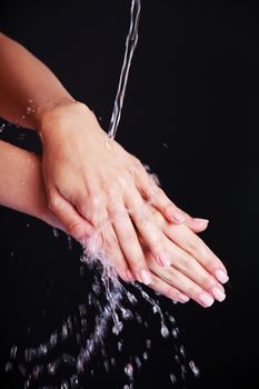 Water falling on female hands, over black background