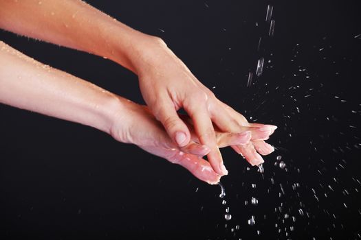 Water falling on female hands, over black background