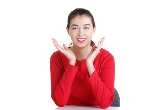 Pretty, happy, young woman in casual clothes sitting at the desk, isolated on white