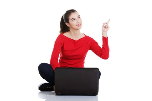 Young pretty woman sitting, working on laptop computer and pointing up on copy space, isolated on white