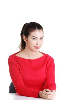 Pretty, happy, young woman in casual clothes sitting at the desk, isolated on white