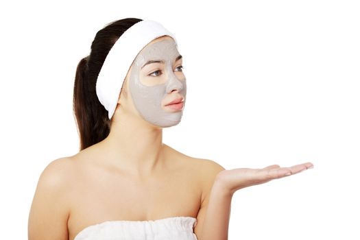 Beautiful woman with clay facial mask showing something on her palm, isolated on white