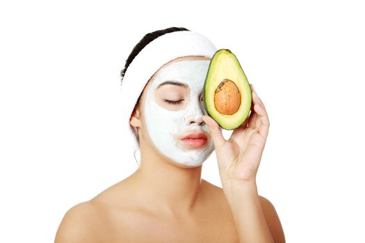 Young woman holding avocado heaving face clay mask on the face in a spa