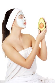 Young woman holding avocado heaving face clay mask on the face in a spa