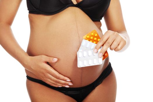 Young beautiful pregnant woman holding pills in front of her belly